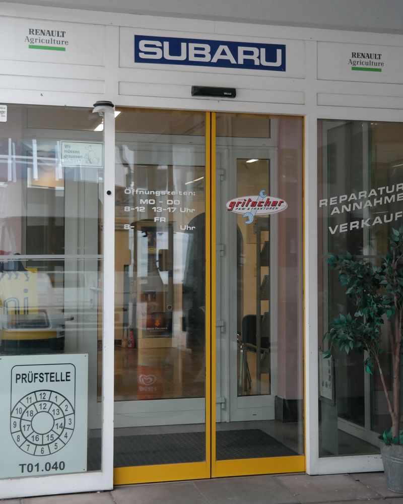 Eingang von KFZ GRITSCHER mit Subaru Schild, Glastür und Prüfstellen-Plakette